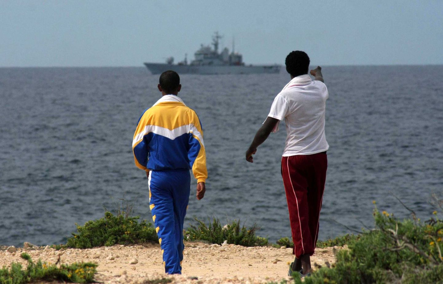 Kaks immigranti vaatamas Lampedusa rannalt merele, kus käivad päästetööd.