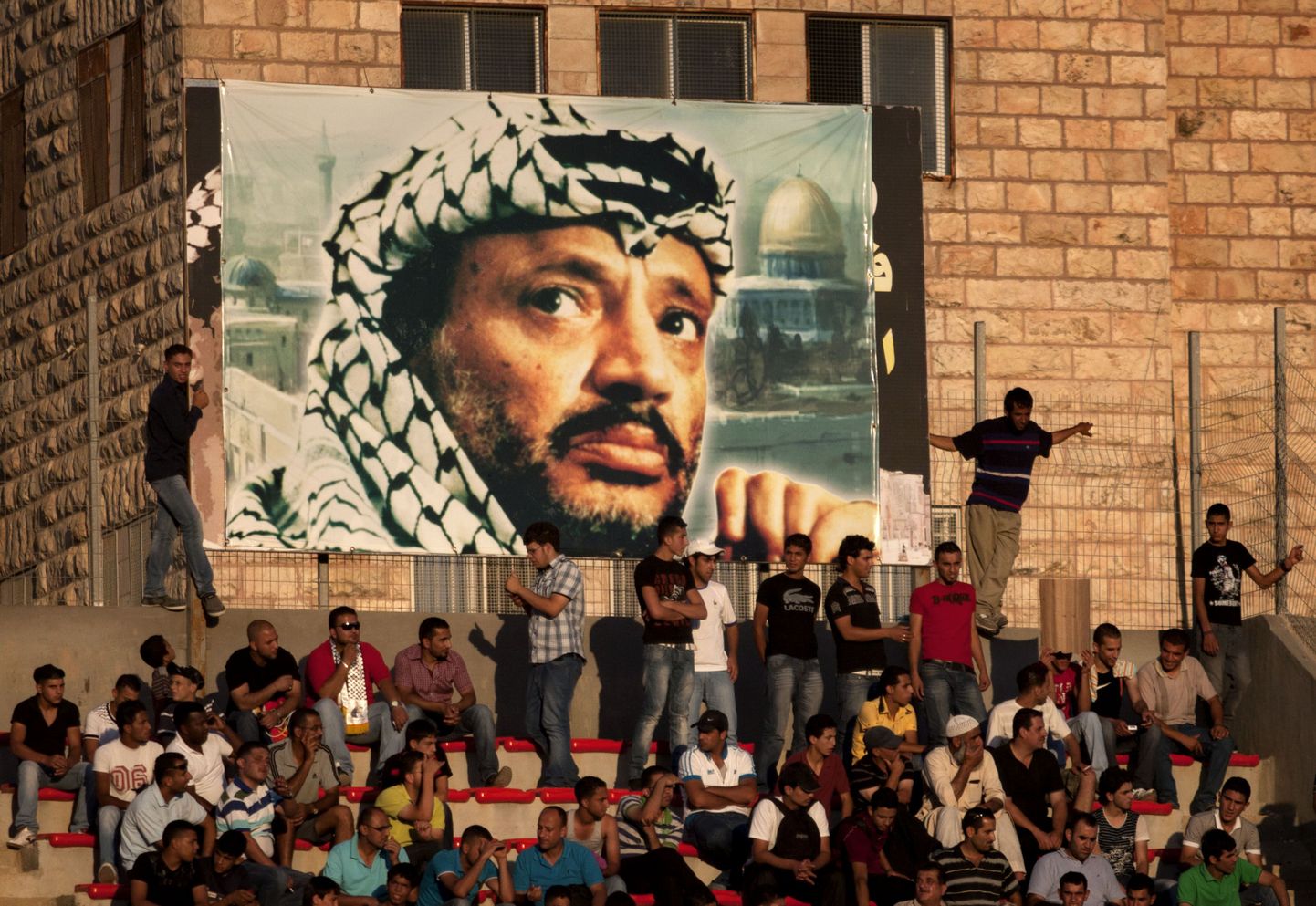 Palestiina jalgpallifännid Yasser Arafati plakati all istumas.