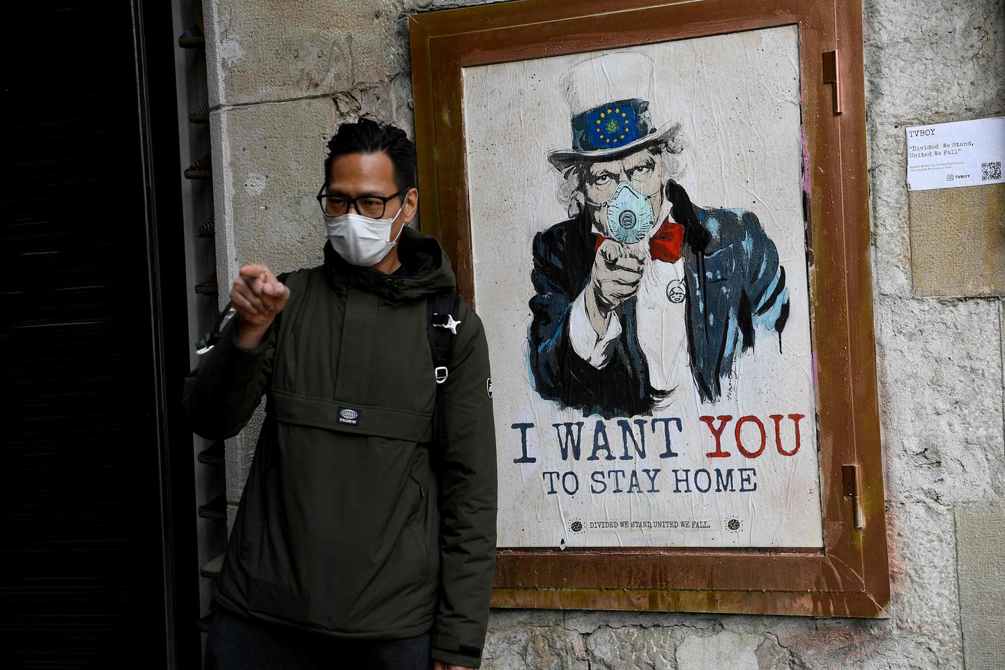 Vīrietis Barselonā pie stilizēta "Tēvoča Sema" plakāta, kas aicina palikt mājās.