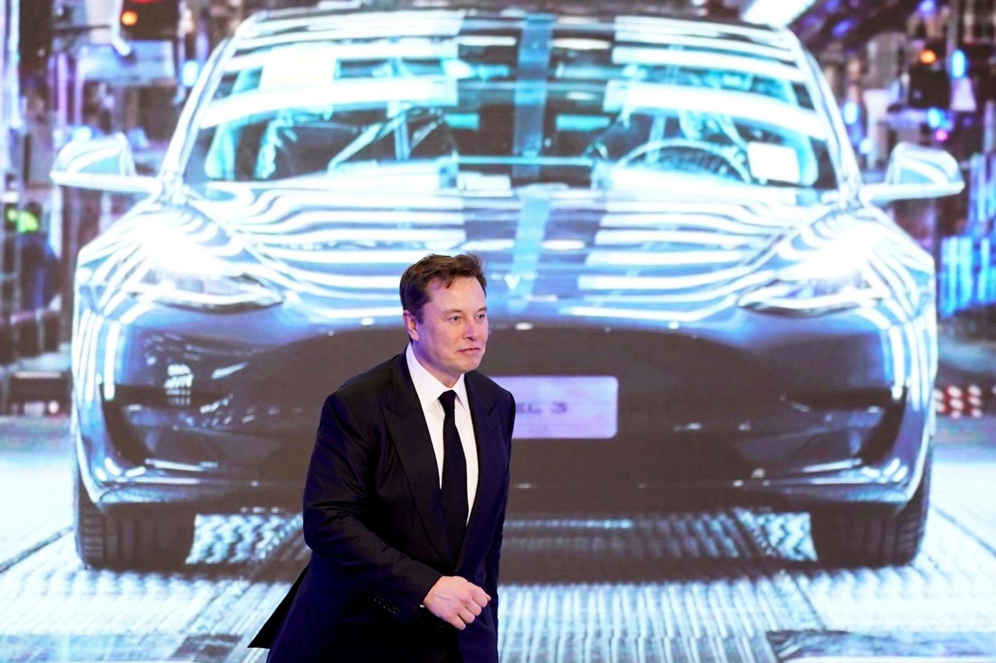 Elon Musk ekraani ees, millel on Tesla sedaan Model 3.