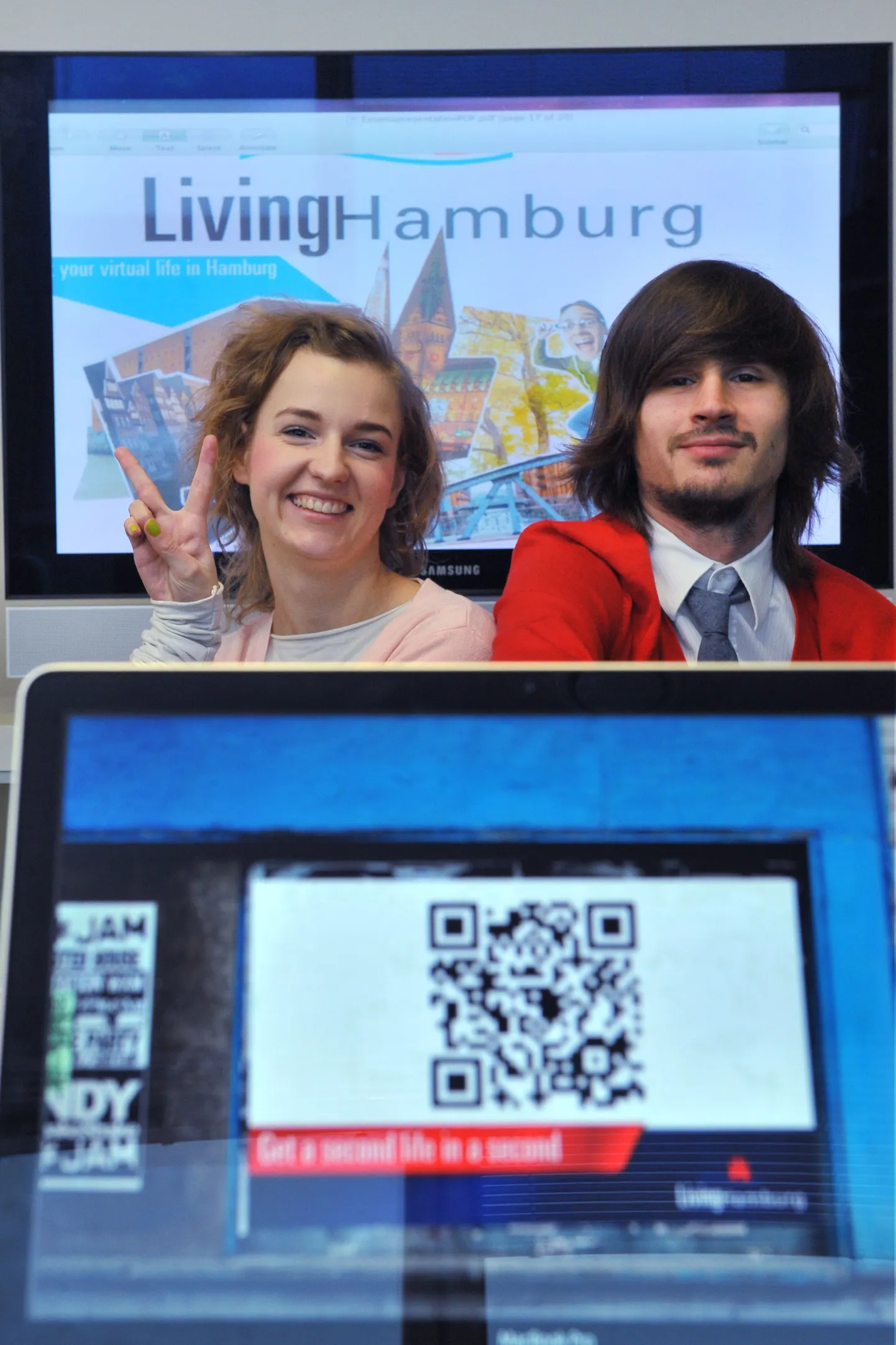 Helene Vetik ja Karl Saluveer. Esiplaanil olevast arvutist on näha artiklis kirjeldatud QR-koodi, taustal ekraanil võistlustöö esitlus