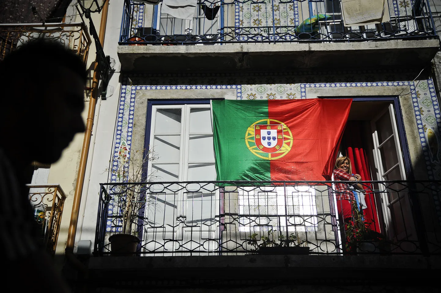TO GO WITH A AFP STORY BY LEVI FERNANDES
A woman watches the performance of the fado singer Pedro Galveias from her balcony that displays the Portugal flag, in Lisbon on July 6, 2012.  Fado singers perform for groups of tourists and local residents during the cultural and tourist program called "Visits sung in Mouraria", Mouraria is one of the typical Lisbon's neighborhoods and is known as the cradle of the Fado, the performances are completed with a guided tour by some places of neighborhood. AFP PHOTO/ PATRICIA DE MELO MOREIRA