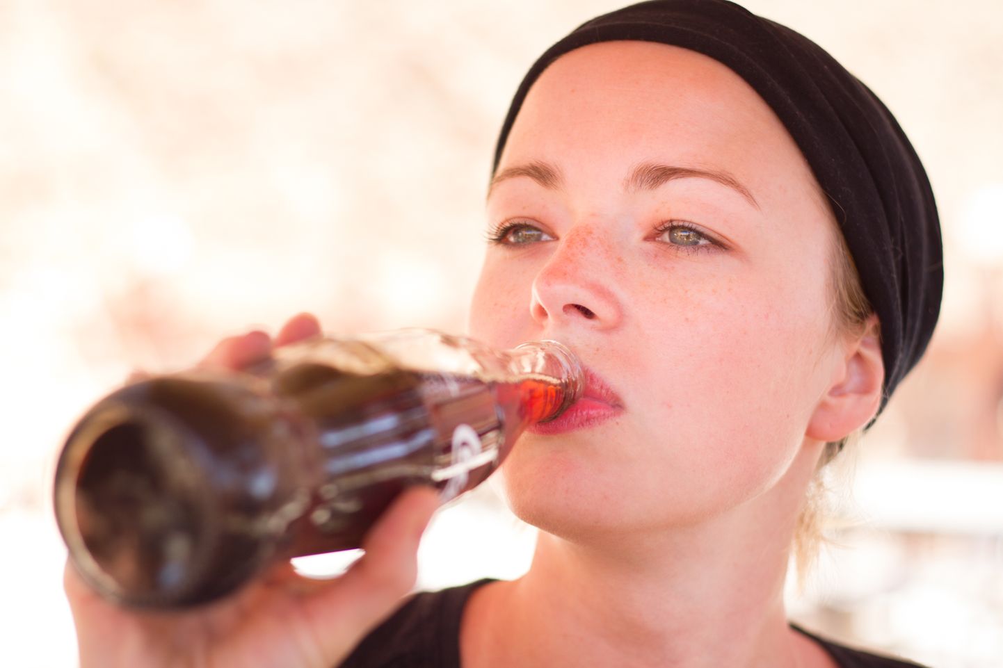 Thirsty active female traveler drinking cola soft dring from glass bottle.