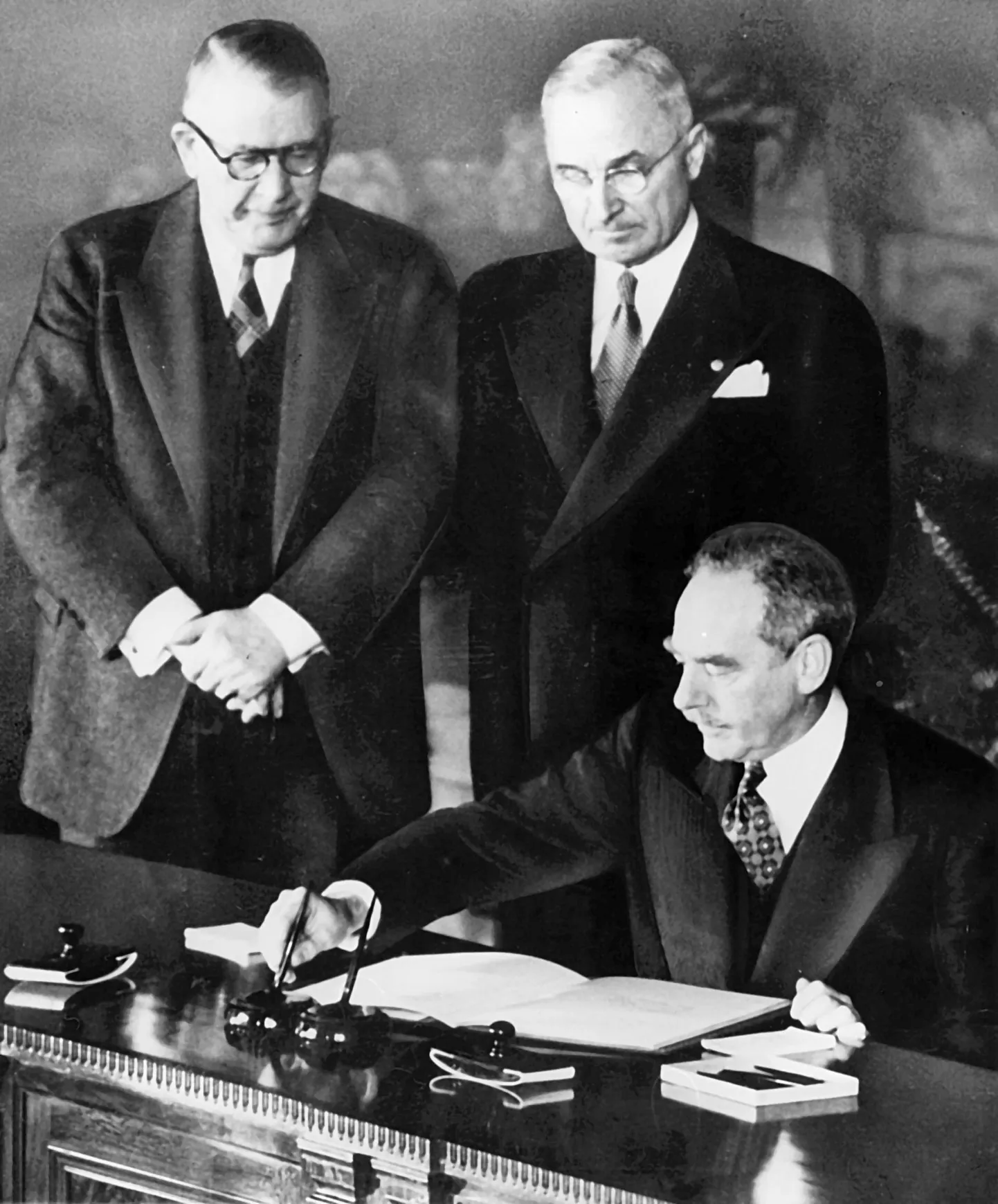 NATO-le aluse pannud Põhja-Atlandi lepingu allkirjastamine 1949. aasta 4. aprillil Washingtonis. Lepingule kirjutab alla Ameerika Ühendriikide välisminister Dean Acheson. Tema taga seisavad Ameerika Ühendriikide asepresident Alben W. Barkley
ja president Harry Truman.