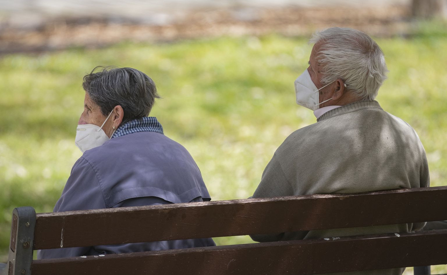 Eakas mees ja naine pargis, kaitstes ennast COVID-19 nakkuse ohu eest maskidega.