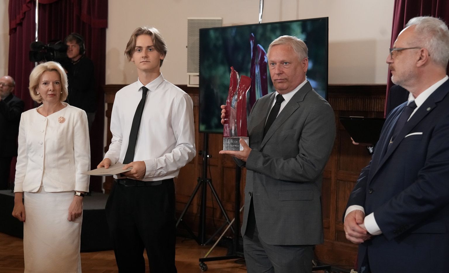 Valsts prezidents Egils Levits (no labās) pasniedz Valstiskuma balvu dzejnieka Knuta Skujenieka dēlam Jānim Skujeniekam un mazdēlam Emīlam Skujeniekam otrās Valstiskuma balvas pasniegšanas svinīgajā ceremonijā.
