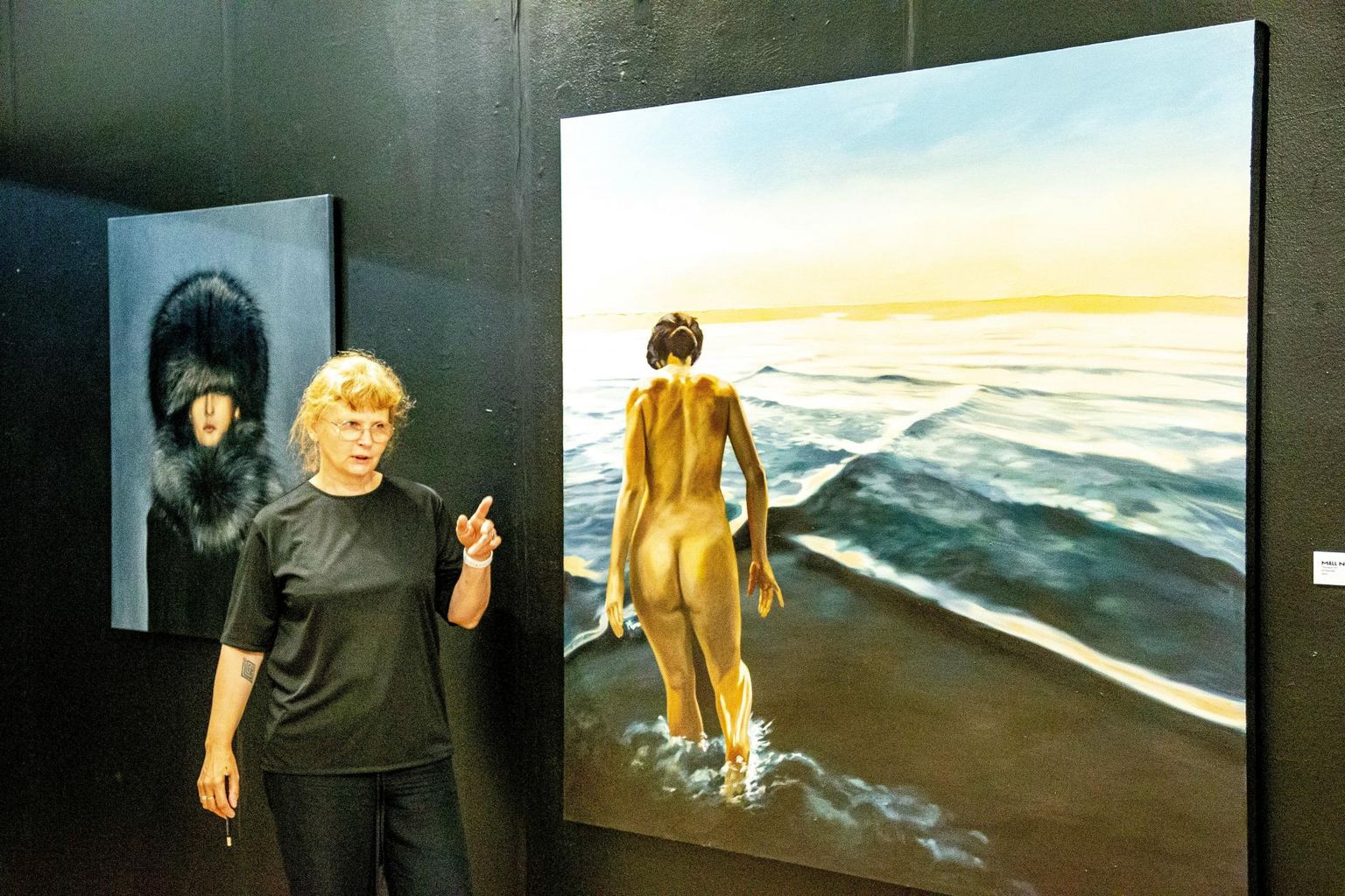 Näituse «7 kunstnikku. Keha» üks kuraatoreid on Mall Nukke, kelle vasakul küljel on tema enda maal «Silmapiir III» ja selja taga Mauri Grossi «Metsik».